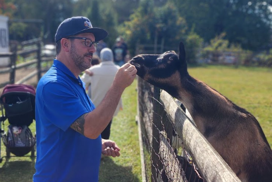 A man feeding a goat in an outdoor setting