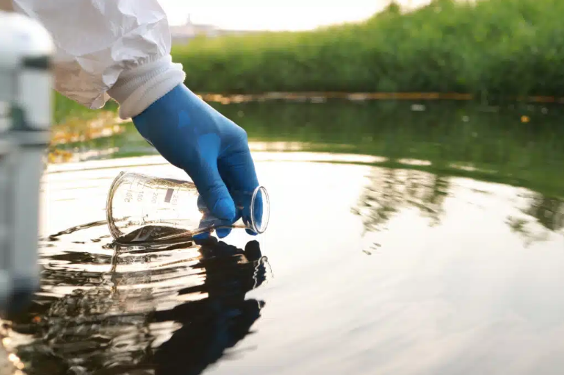 gloved hand collecting water for a pond in beaker