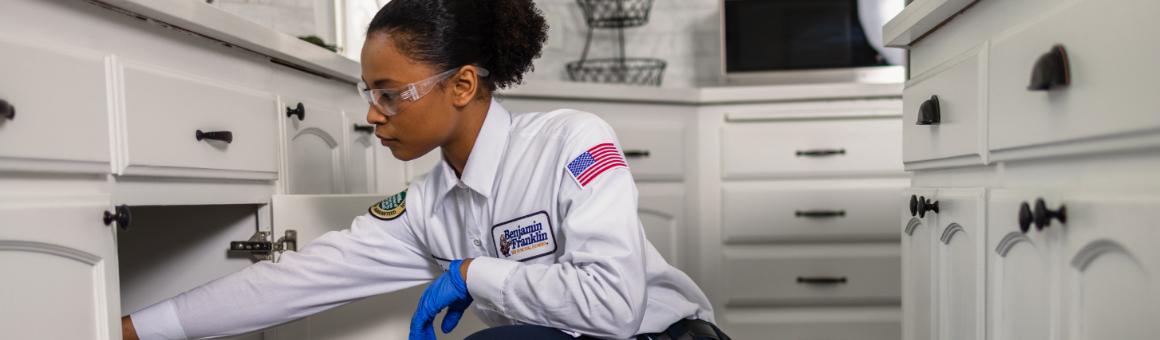 Plumbing professional inspecting the inside of a kitchen cabinet.
